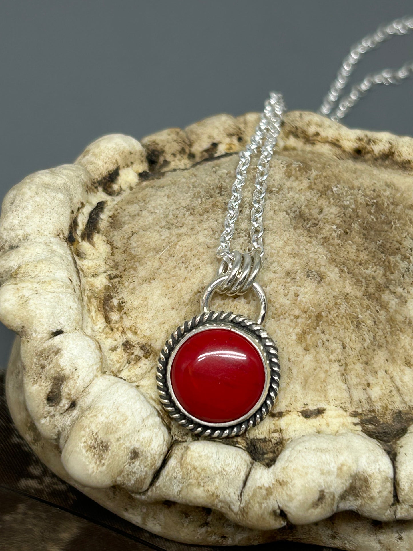 Round red Rosarita set in sterling silver accented with sterling silver twist wire. This pendant is 5/8 of an inch in diameter and hangs on an 18 inch sterling silver chain.