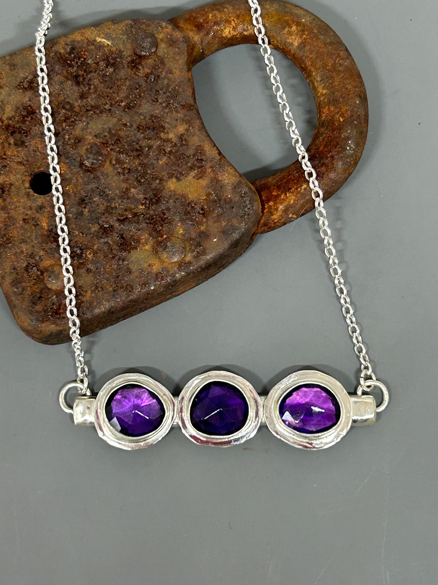 Three pieces of rose cut amethyst set in sterling silver on a sterling silver bar with a shiny finish. This necklace is 18 inches long.