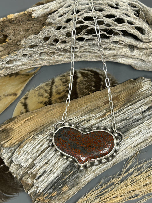 Heart shaped dinosaur bone shaped heart set in sterling silver accented with sterling silver dots. This pendant hangs on an 18 inch chain.