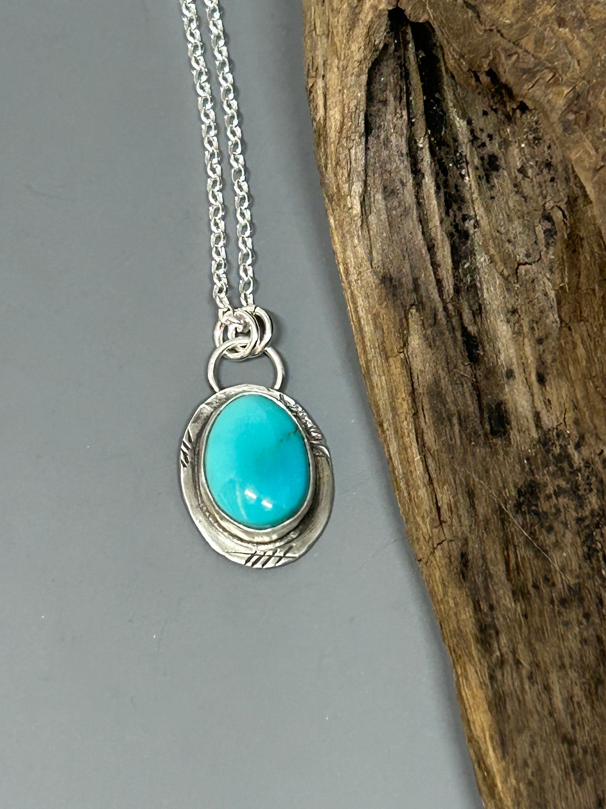 Blue oval Royston turquoise set in a distressed silver setting and hangs on an 18 inch sterling silver chain.