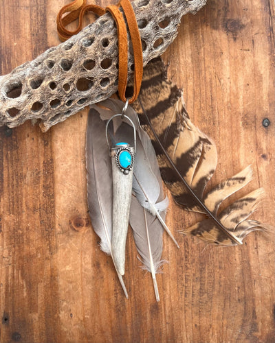 Naturally shed deer antler set in sterling silver accented with two Moronic turquoise stones.  This pendant hangs on 38 inches of soft brown leather.